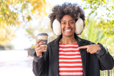 African American girl wearing winter muffs while holding a coffee at outdoors with surprise facial expression