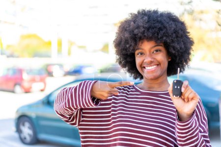 Téléchargez les photos : Afro-américaine fille tenant des clés de voiture à l'extérieur et pointant vers elle - en image libre de droit