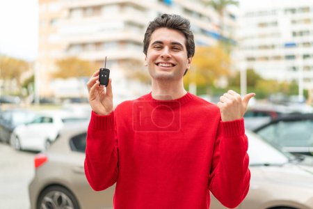 Téléchargez les photos : Jeune homme beau avec clé de voiture pointant vers le côté pour présenter un produit - en image libre de droit