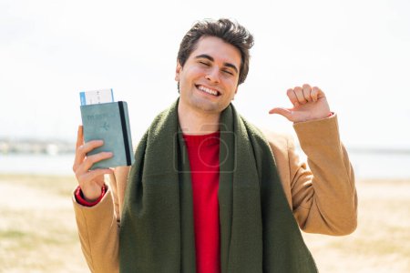 Téléchargez les photos : Jeune homme beau tenant un passeport à l'extérieur fier et satisfait de soi - en image libre de droit