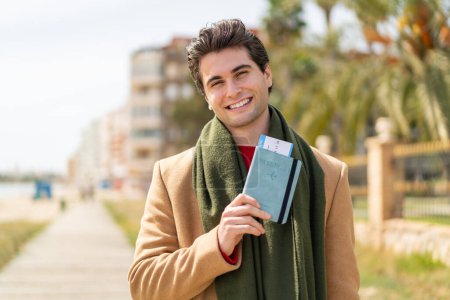 Téléchargez les photos : Jeune homme beau tenant un passeport avec une expression heureuse - en image libre de droit