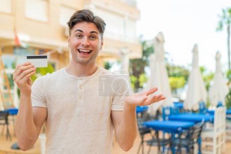 Photo for Young handsome man holding a credit card at outdoors with shocked facial expression - Royalty Free Image