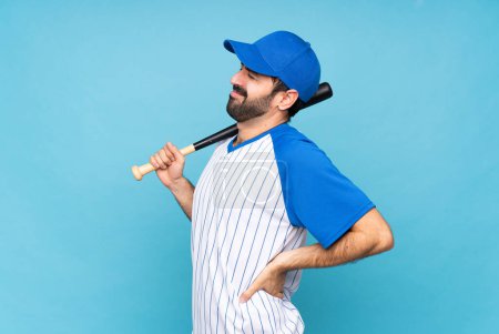 Foto de Joven jugando béisbol sobre fondo azul aislado sufriendo de dolor de espalda por haber hecho un esfuerzo - Imagen libre de derechos