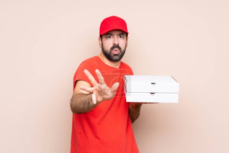 Téléchargez les photos : Jeune homme tenant une pizza sur fond isolé nerveux étirant les mains vers l'avant - en image libre de droit