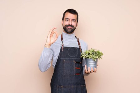Photo for Man holding a plant over isolated background showing ok sign with fingers - Royalty Free Image