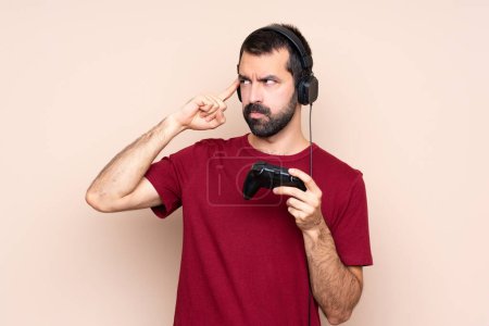Téléchargez les photos : Homme jouant avec un contrôleur de jeu vidéo sur mur isolé ayant des doutes et la pensée - en image libre de droit