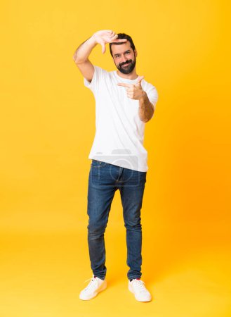 Photo for Full-length shot of man with beard over isolated yellow background focusing face. Framing symbol - Royalty Free Image