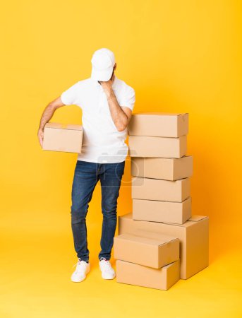 Photo for Full-length shot of delivery man among boxes over isolated yellow background with tired and sick expression - Royalty Free Image
