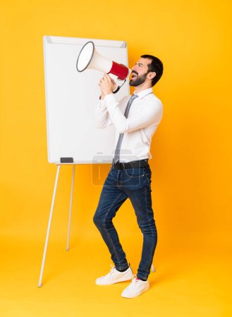 Photo for Full-length shot of businessman giving a presentation on white board over isolated yellow background shouting through a megaphone - Royalty Free Image