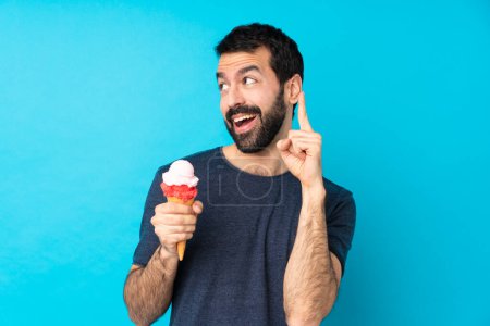 Téléchargez les photos : Jeune homme avec une crème glacée cornet sur fond bleu isolé dans le but de réaliser la solution tout en levant le doigt - en image libre de droit