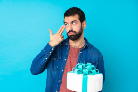 Photo for Young handsome man with a big cake over isolated blue background with problems making suicide gesture - Royalty Free Image