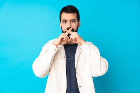 Photo for Young handsome man with white corduroy jacket over isolated blue background showing a sign of silence gesture - Royalty Free Image