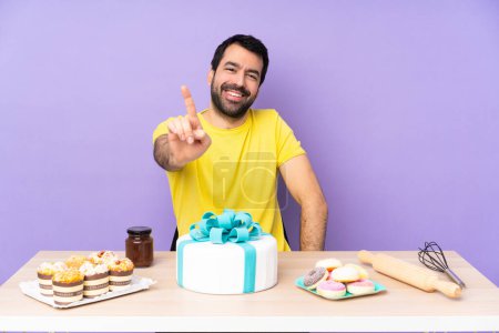 Téléchargez les photos : Homme dans une table avec un gros gâteau montrant et levant un doigt - en image libre de droit