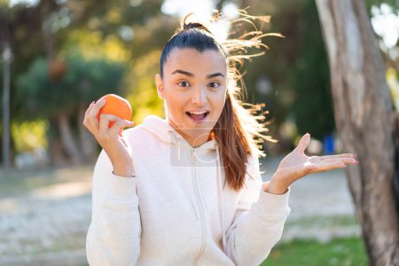 Photo for Young pretty brunette woman holding an orange at outdoors with shocked facial expression - Royalty Free Image