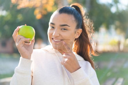 Téléchargez les photos : Jeune jolie femme sportive tenant une pomme avec une expression heureuse - en image libre de droit