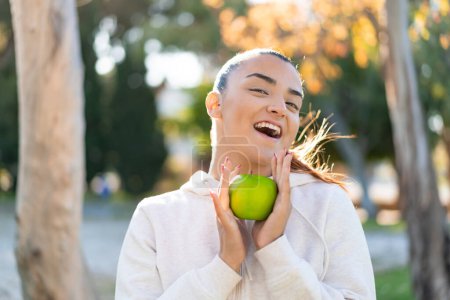 Foto de Joven mujer bastante deportiva sosteniendo una manzana con expresión sorprendida - Imagen libre de derechos