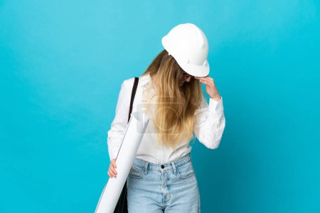 Téléchargez les photos : Jeune architecte femme avec casque et tenant des plans isolés sur fond bleu riant - en image libre de droit