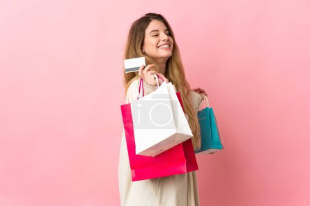 Téléchargez les photos : Jeune femme avec sac isolé sur fond rose tenant des sacs à provisions et une carte de crédit - en image libre de droit