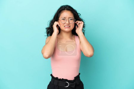 Foto de Joven asiático mujer aislado en azul fondo frustrado y cubriendo orejas - Imagen libre de derechos