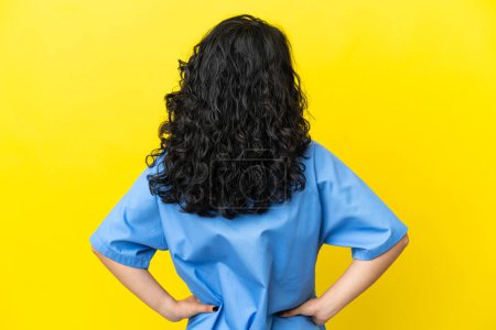 Téléchargez les photos : Jeune chirurgien médecin asiatique femme isolée sur fond jaune en position arrière - en image libre de droit