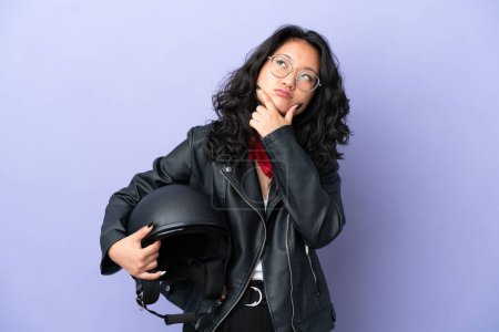 Photo for Young asian woman with a motorcycle helmet isolated on purple background having doubts - Royalty Free Image