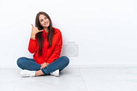 Téléchargez les photos : Jeune femme ukrainienne assise sur le sol isolé sur fond blanc faisant geste de téléphone. Rappelle-moi signe - en image libre de droit