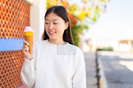 Téléchargez les photos : Jolie femme chinoise avec une crème glacée cornet à l'extérieur avec une expression heureuse - en image libre de droit