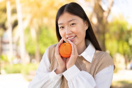 Téléchargez les photos : Jolie Chinoise en plein air tenant une orange - en image libre de droit