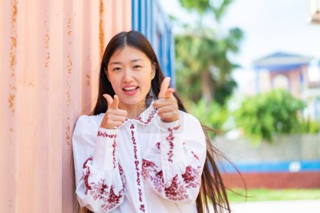 Foto de Joven mujer china al aire libre señalando hacia el frente y sonriendo - Imagen libre de derechos