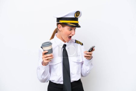 Photo for Airplane caucasian pilot woman isolated on white background holding coffee to take away and a mobile - Royalty Free Image