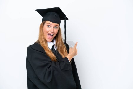 Téléchargez les photos : Jeune diplômée universitaire femme caucasienne isolée sur fond blanc surpris et pointant côté - en image libre de droit