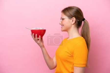Téléchargez les photos : Jeune femme caucasienne tenant un bol de céréales isolé sur fond rose avec une expression heureuse - en image libre de droit