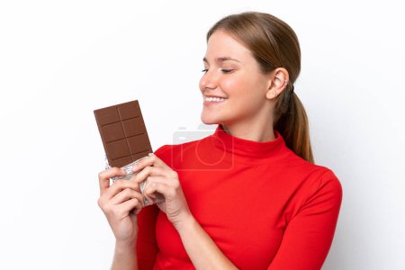 Jeune femme caucasienne isolée sur fond blanc prenant une tablette de chocolat et heureuse