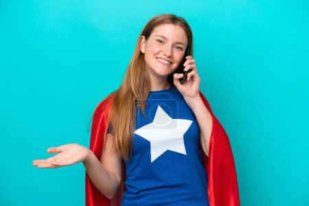 Foto de Super Héroe mujer caucásica aislada sobre fondo azul manteniendo una conversación con el teléfono móvil con alguien - Imagen libre de derechos