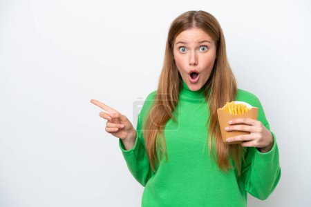 Téléchargez les photos : Jeune femme caucasienne tenant des frites isolées sur fond blanc surpris et pointant côté - en image libre de droit