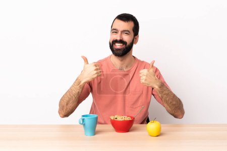 Foto de Caucásico hombre desayunando en una mesa dando un gesto pulgar hacia arriba. - Imagen libre de derechos