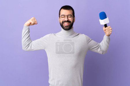 Téléchargez les photos : Reporter adulte homme avec barbe tenant un microphone sur fond violet isolé faisant un geste fort - en image libre de droit