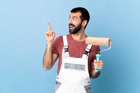 Téléchargez les photos : Peintre adulte homme sur fond bleu isolé dans le but de réaliser la solution tout en levant le doigt - en image libre de droit