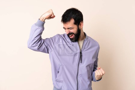 Téléchargez les photos : Homme caucasien avec barbe portant une veste sur fond isolé célébrant une victoire - en image libre de droit
