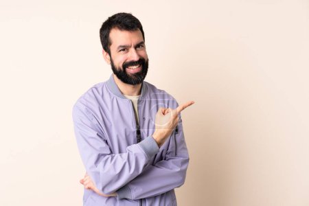 Téléchargez les photos : Homme caucasien avec barbe portant une veste sur fond isolé pointant vers le côté pour présenter un produit - en image libre de droit
