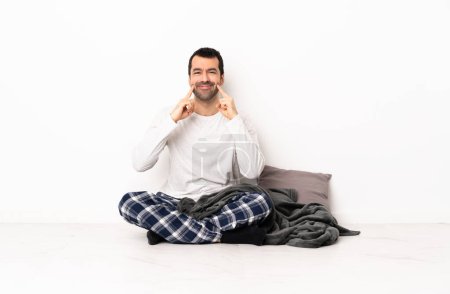 Foto de Hombre caucásico en pijama sentado en el suelo en el interior sonriendo con una expresión feliz y agradable - Imagen libre de derechos