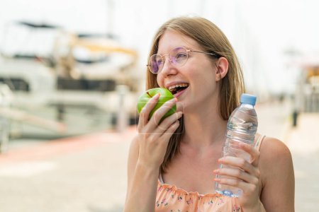Téléchargez les photos : Jeune fille française avec des lunettes à l'extérieur avec une pomme et une bouteille d'eau - en image libre de droit