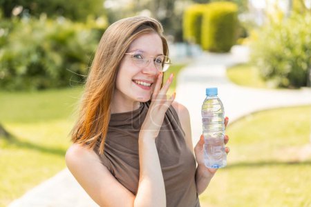 Foto de Chica francesa con vasos sosteniendo una botella de agua al aire libre susurrando algo - Imagen libre de derechos