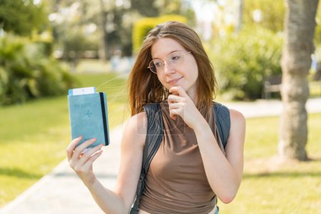 Téléchargez les photos : Jeune fille française avec des lunettes à l'extérieur tenant un passeport et pensant - en image libre de droit