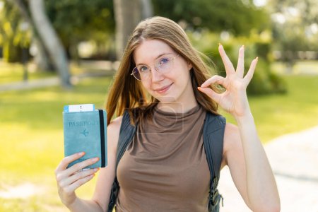 Photo for French girl with glasses holding a passport at outdoors showing ok sign with fingers - Royalty Free Image