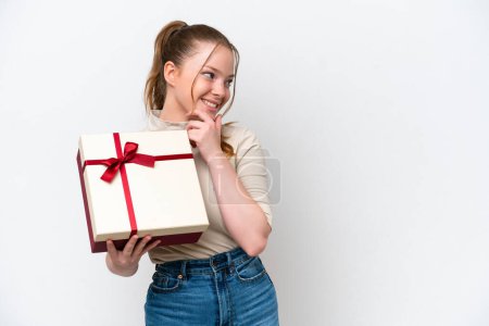 Téléchargez les photos : Young caucasian woman holding a gift isolated on white background thinking an idea and looking side - en image libre de droit