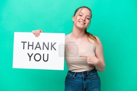 Young caucasian woman isolated on green background holding a placard with text THANK YOU and  pointing it
