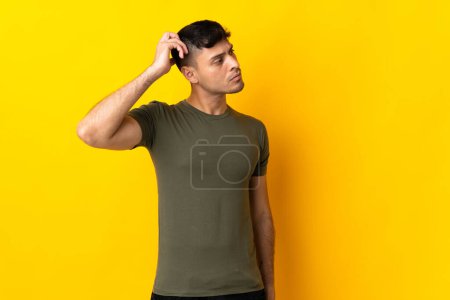 Photo for Young Colombian man isolated on yellow background having doubts while scratching head - Royalty Free Image