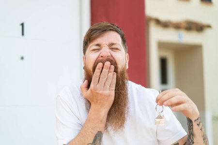 Téléchargez les photos : Homme rousse avec barbe tenant les clés de la maison avec une expression heureuse - en image libre de droit