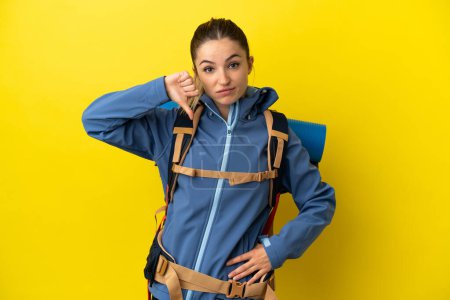 Photo for Young mountaineer woman with a big backpack over isolated yellow background showing thumb down with negative expression - Royalty Free Image